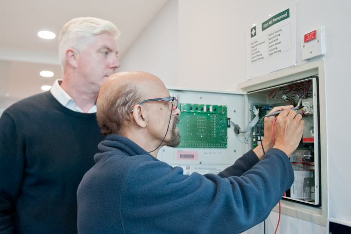 Fire alarm maintenance: two fire alarm engineers examining the inside of a fire alarm panel.