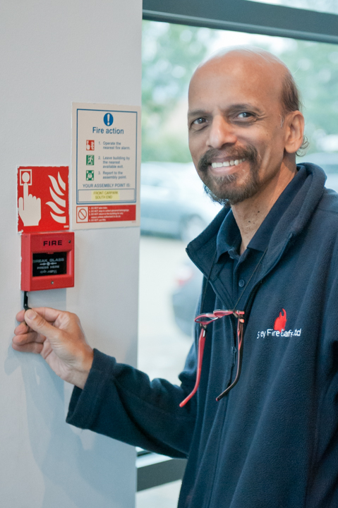 Fire alarm testing: smiling engineer in front of a fire alarm break glass unit.